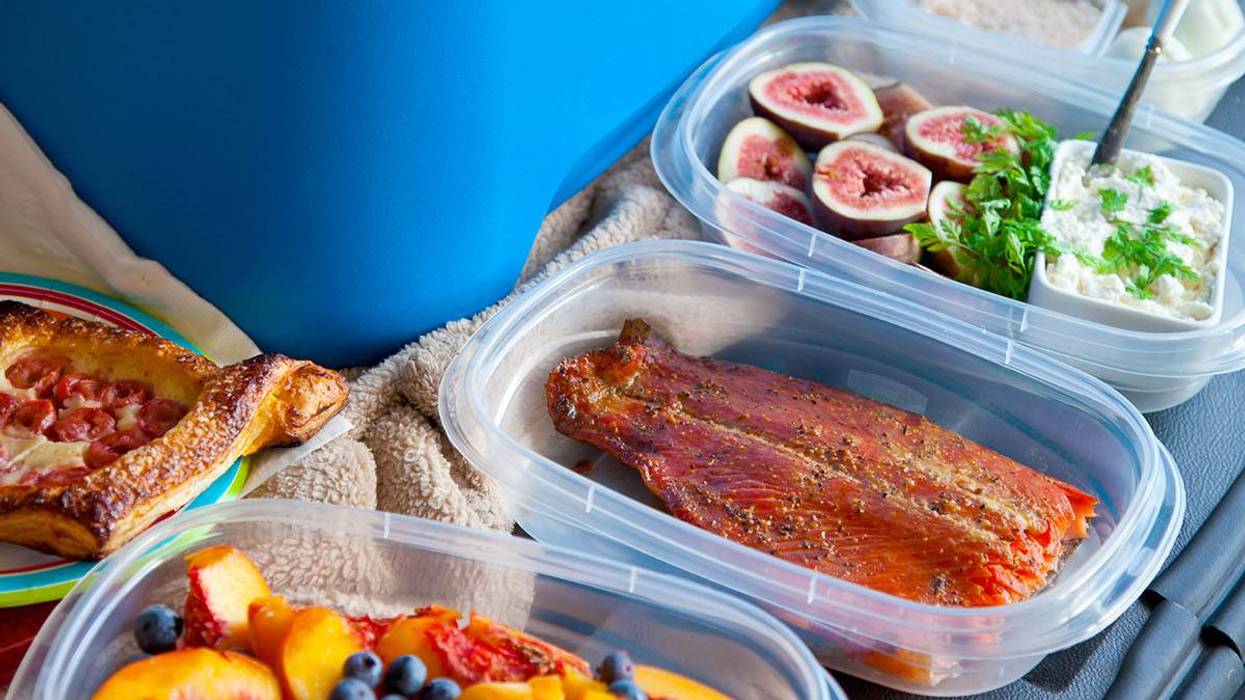 A blue cooler surrounded by plastic containers of fruit, salmon, and other prepared food.