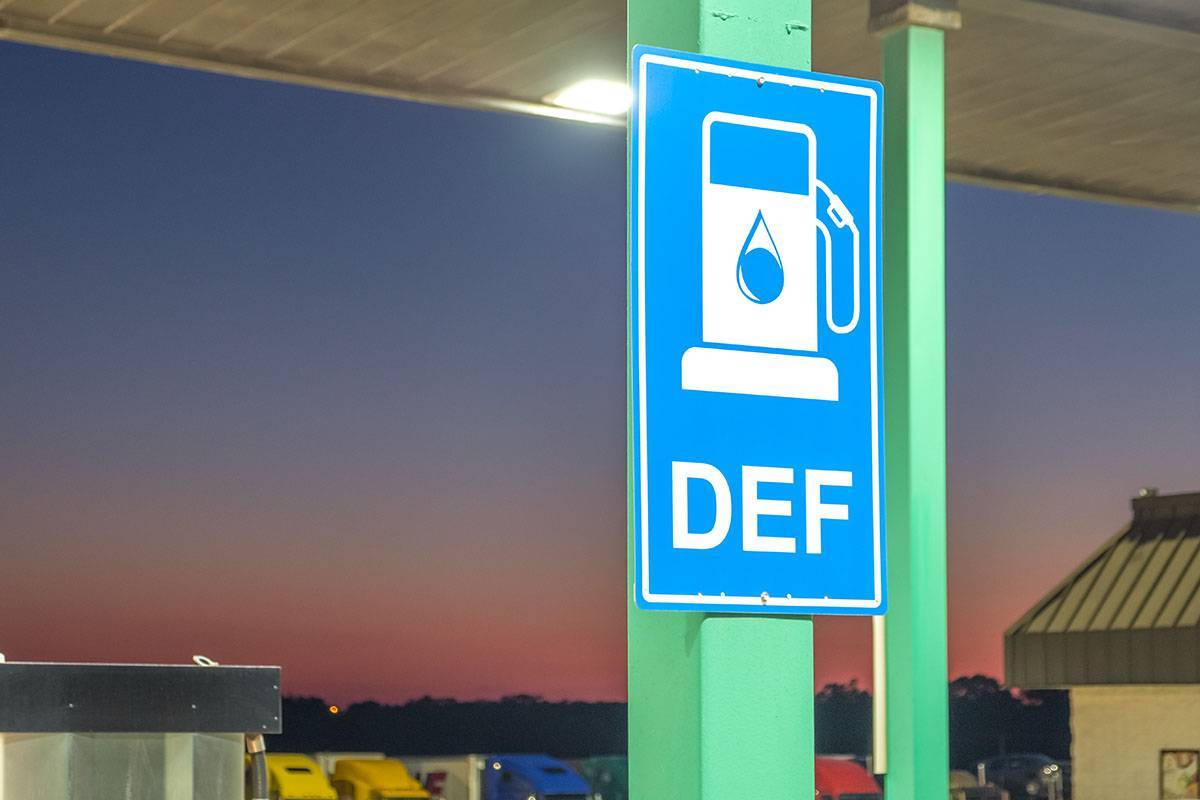 A blue DEF sign hanging on a green post at a fuel station.