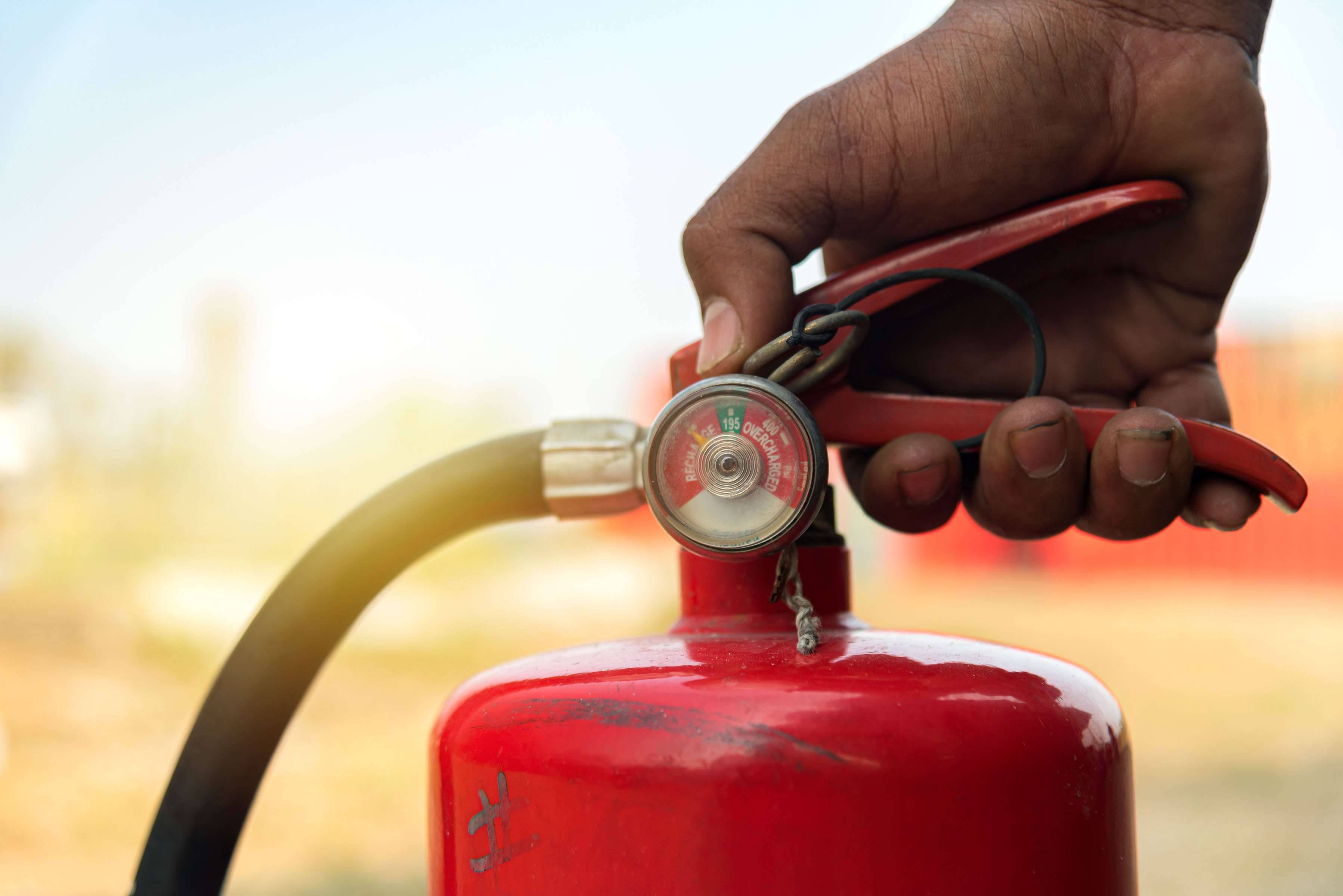 A closeup of a hand on the handle of a red fire extinguisher.