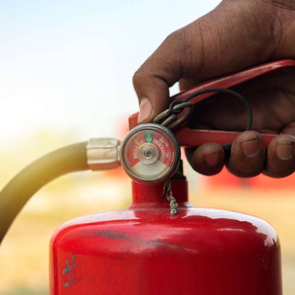 A closeup of a hand on the handle of a red fire extinguisher.
