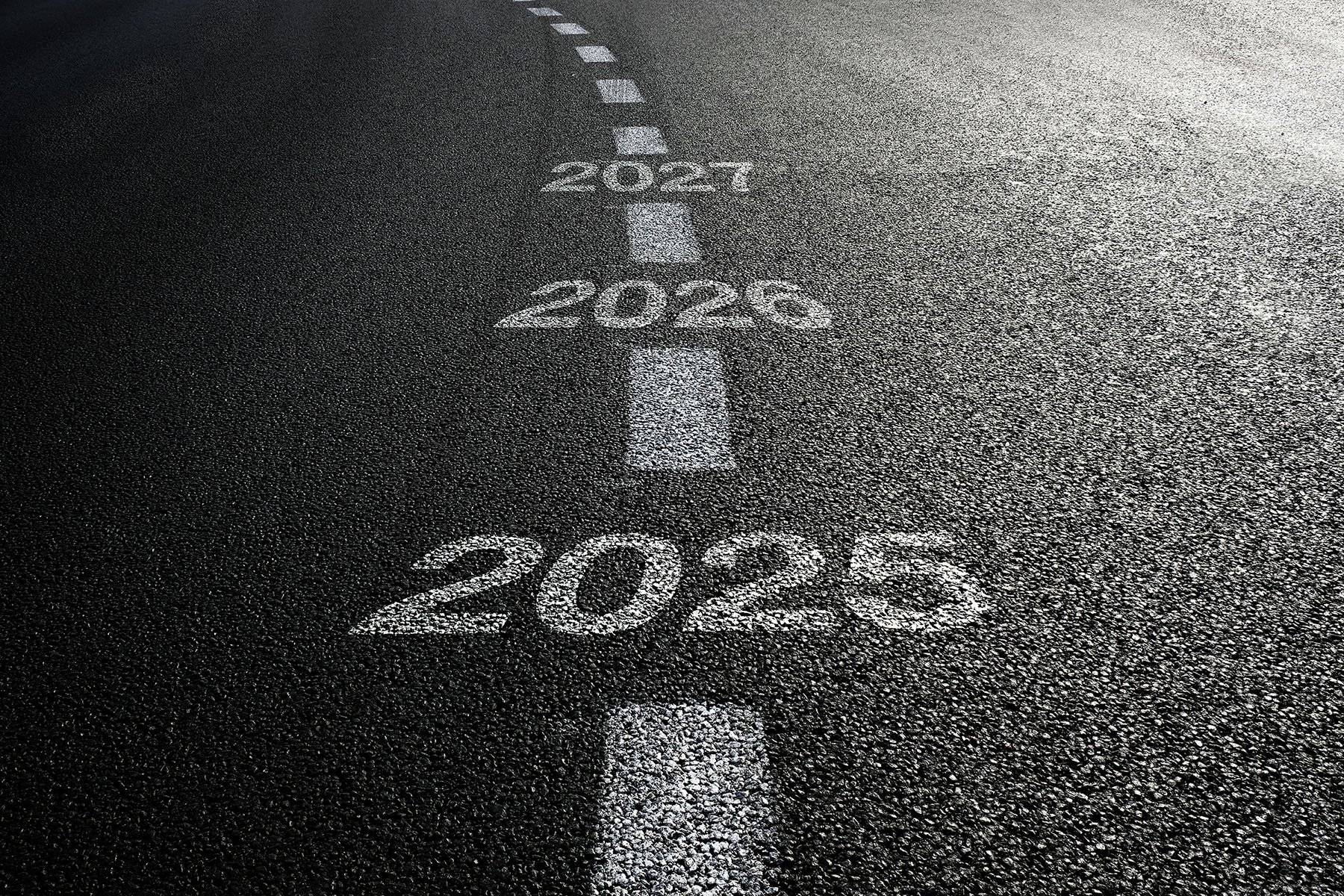 A closeup of as asphalt road with the years 2025, 2026, and 2027 painted on it.
