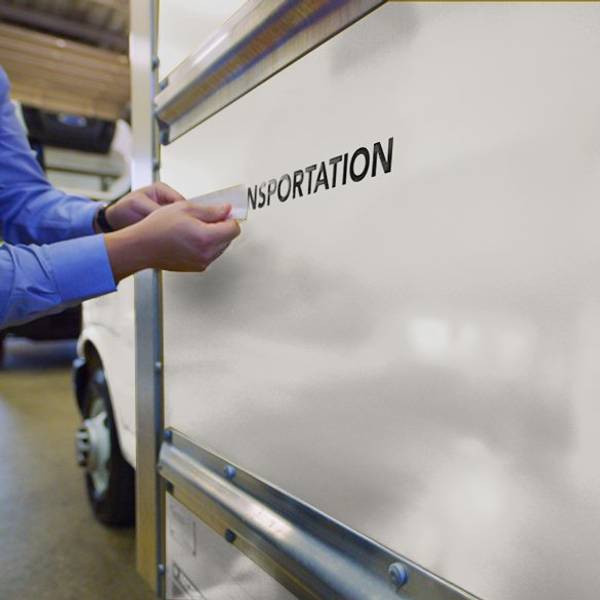 A closeup of hands putting a logo onto the side of a white box truck.