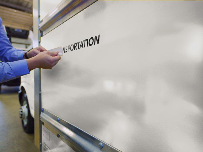 A closeup of hands putting a logo onto the side of a white box truck.