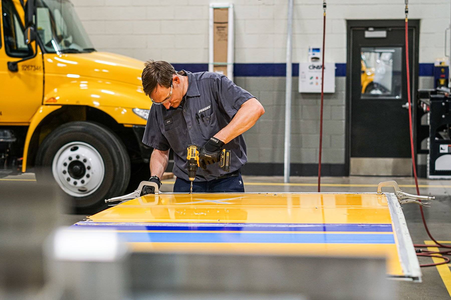 A collision repair technician works on a yellow truck door.