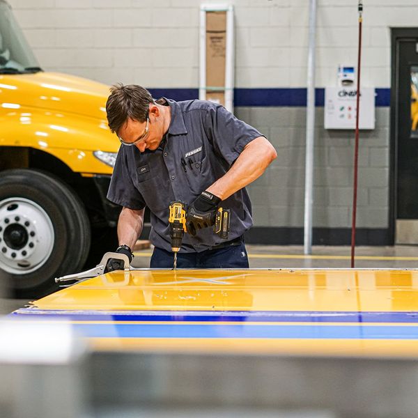 A collision repair technician works on a yellow truck door.