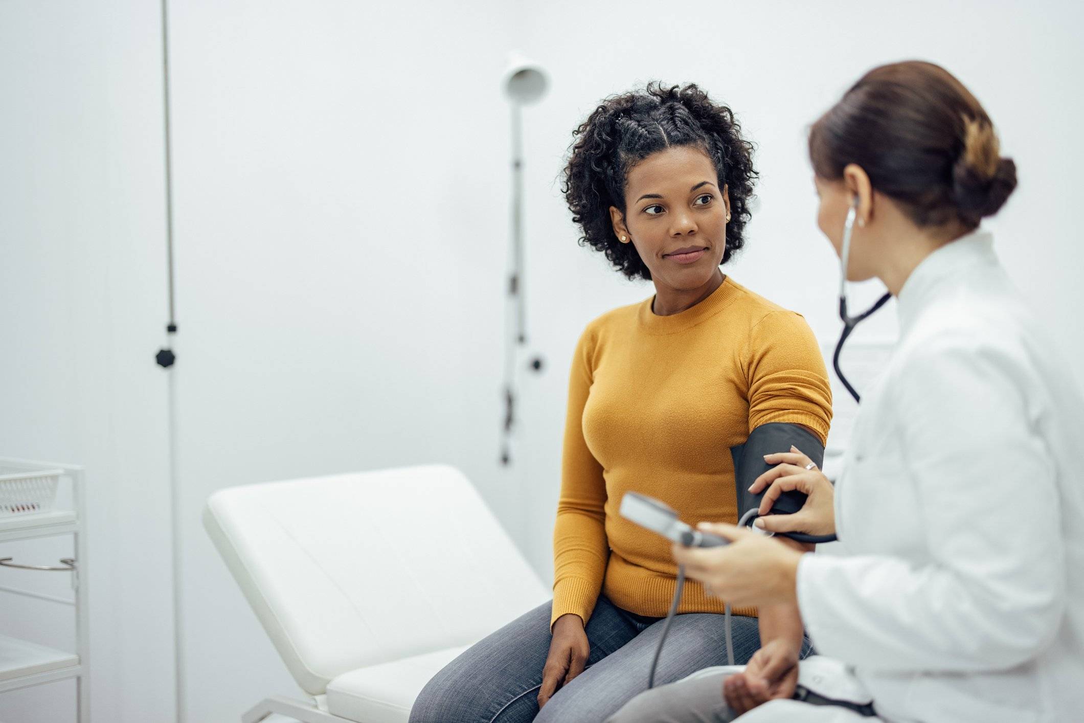 A doctor uses a stethoscope and blood pressure cuff to take a female patient's blood pressure.