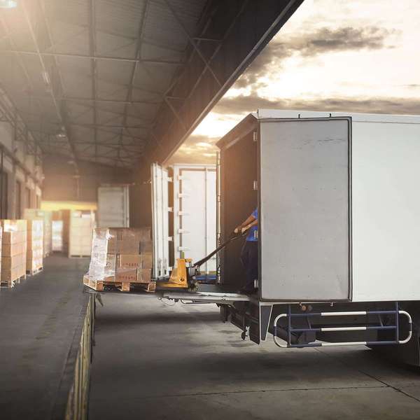 A driver unloads a pallet of boxes from a white semi-truck to a loading dock.
