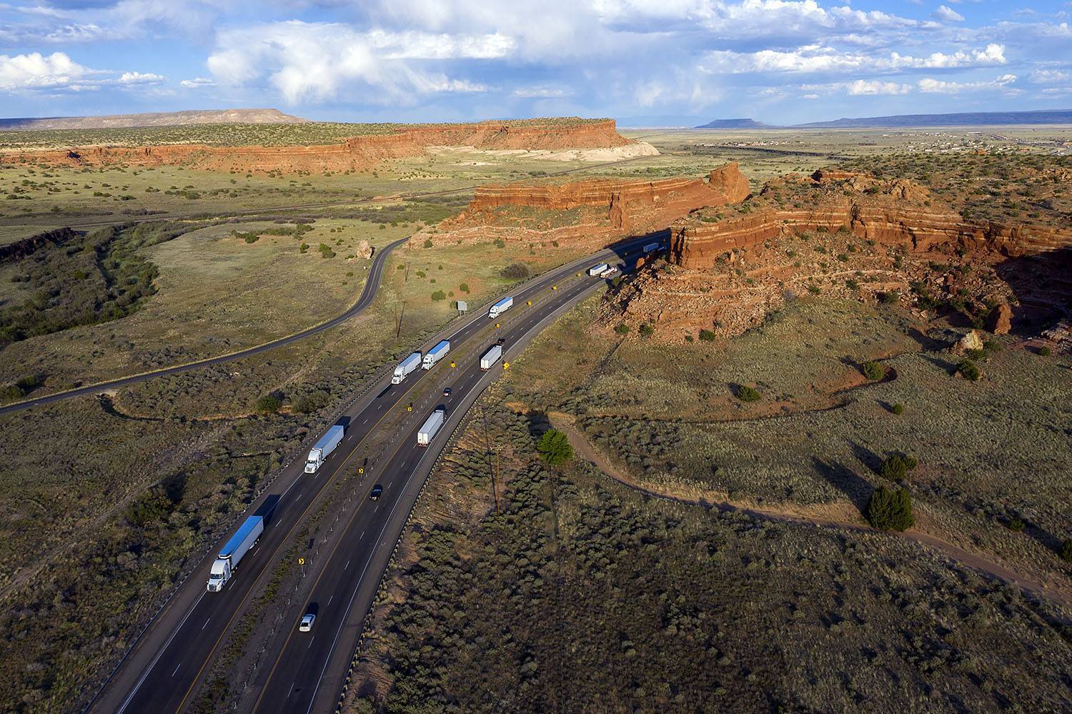 A drone-style image of multiple semi-trucks driving through a Utah landscape against blue skies.
