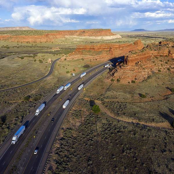 A drone-style image of multiple semi-trucks driving through a Utah landscape against blue skies.