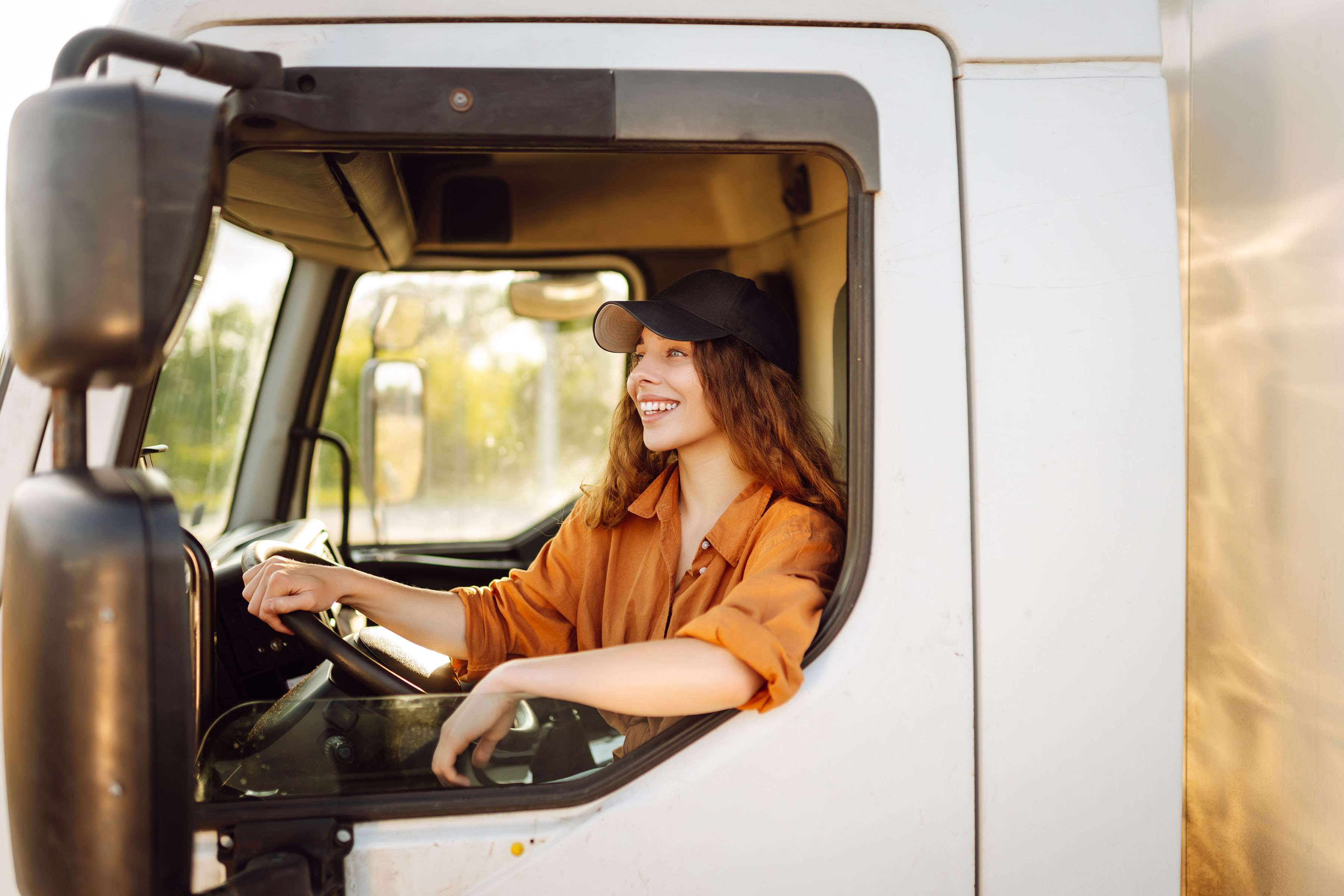 A female truck driver sits in the driver's seat of a white truck.