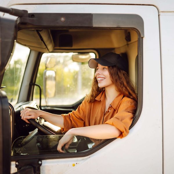 A female truck driver sits in the driver's seat of a white truck.