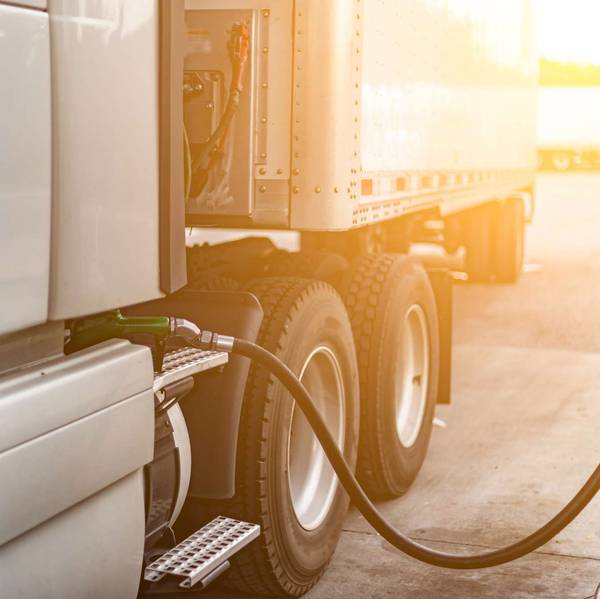 A fuel pump pumps fuel into a semi-truck while the sun sets.