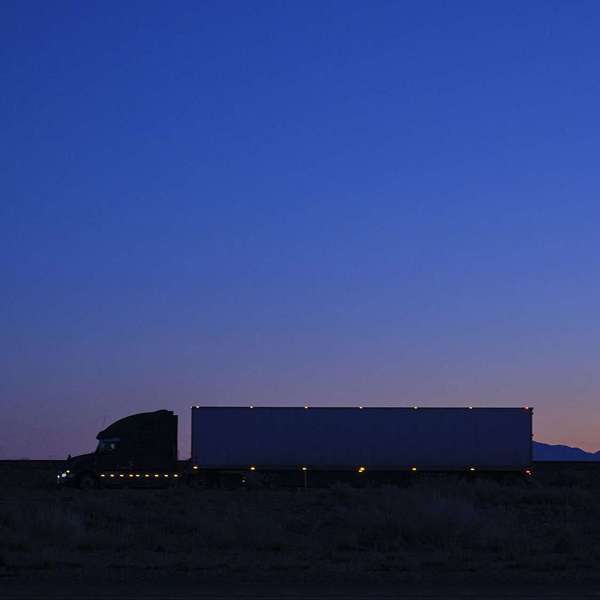 A full shot of a semi-truck with lights driving at dusk.