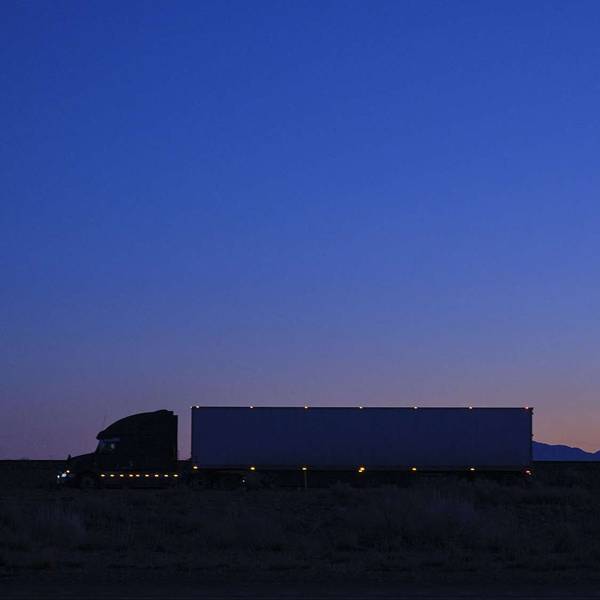 A full shot of a semi-truck with lights driving at dusk.