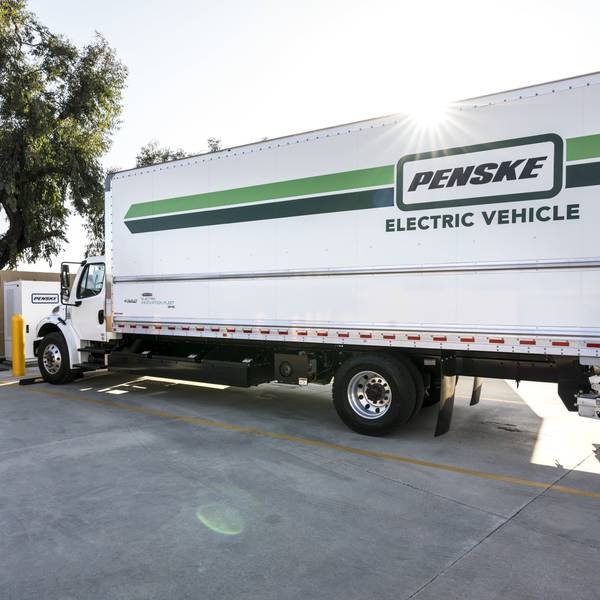 A green and white Penske Electric Box Truck parked at a charging station.