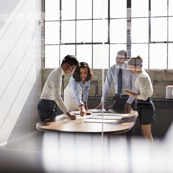 A group of four executives stand around a table looking at files and papers.