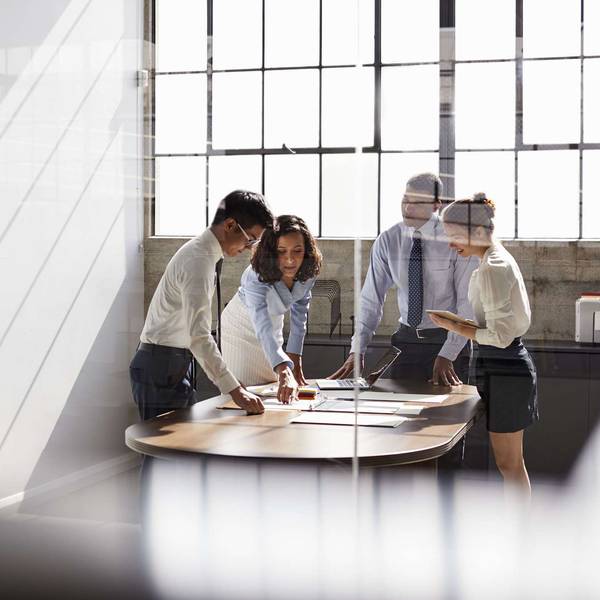 A group of four executives stand around a table looking at files and papers.