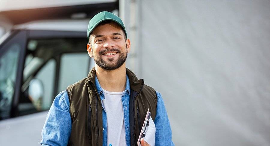 A happy male trucker stands in front of his white truck.