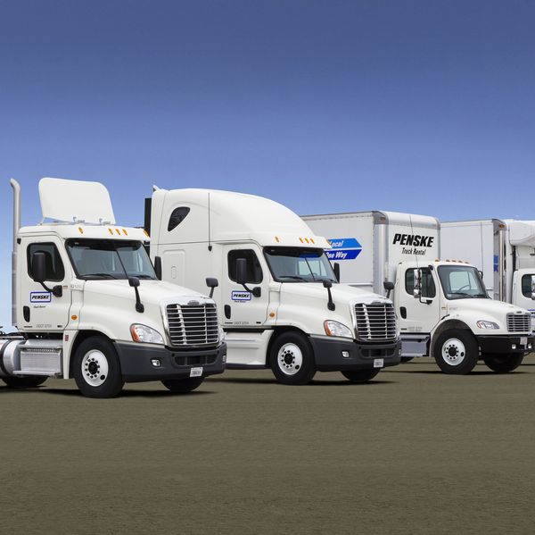 A lineup of four white Penske Leasing trucks.