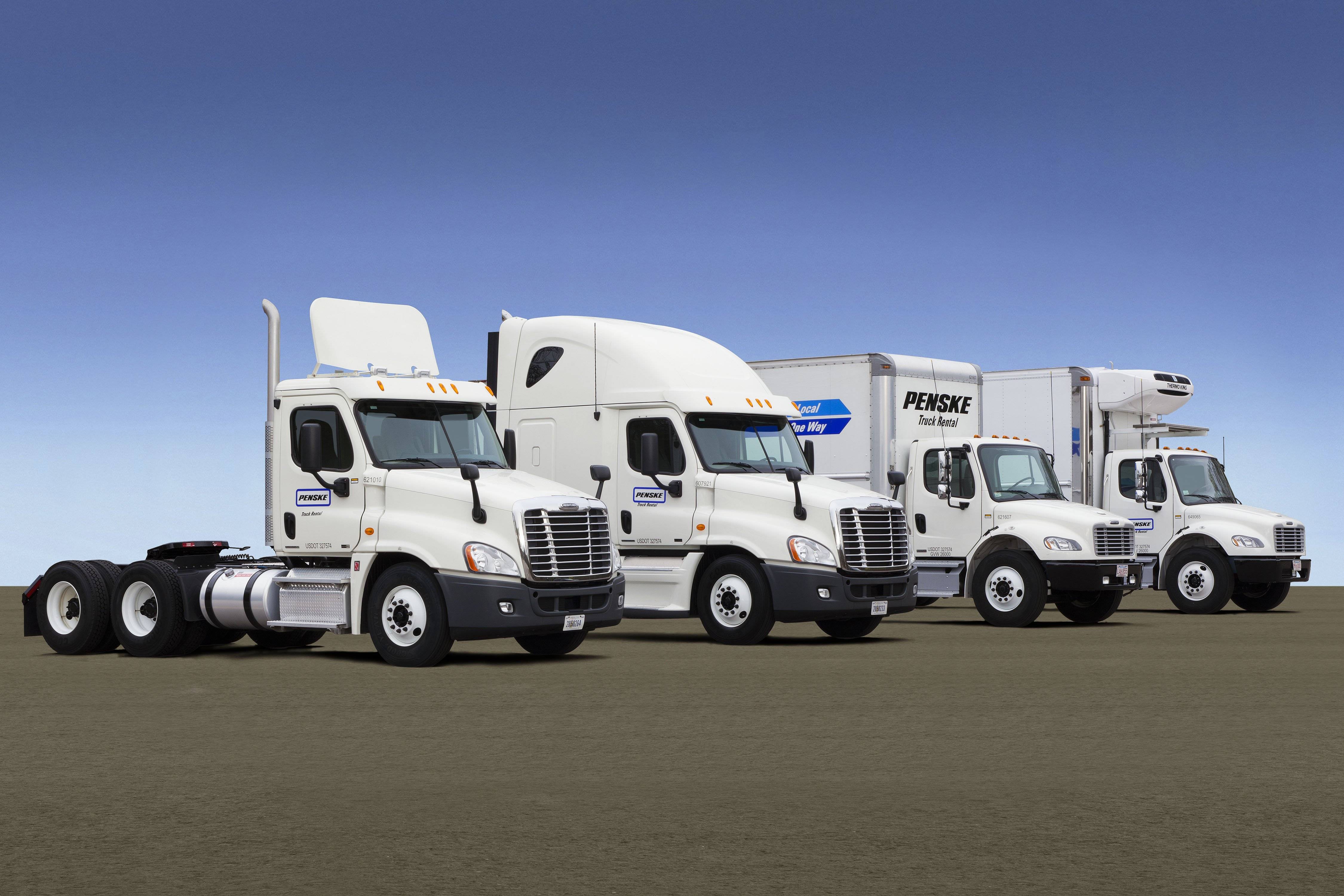 A lineup of four white Penske Leasing trucks.