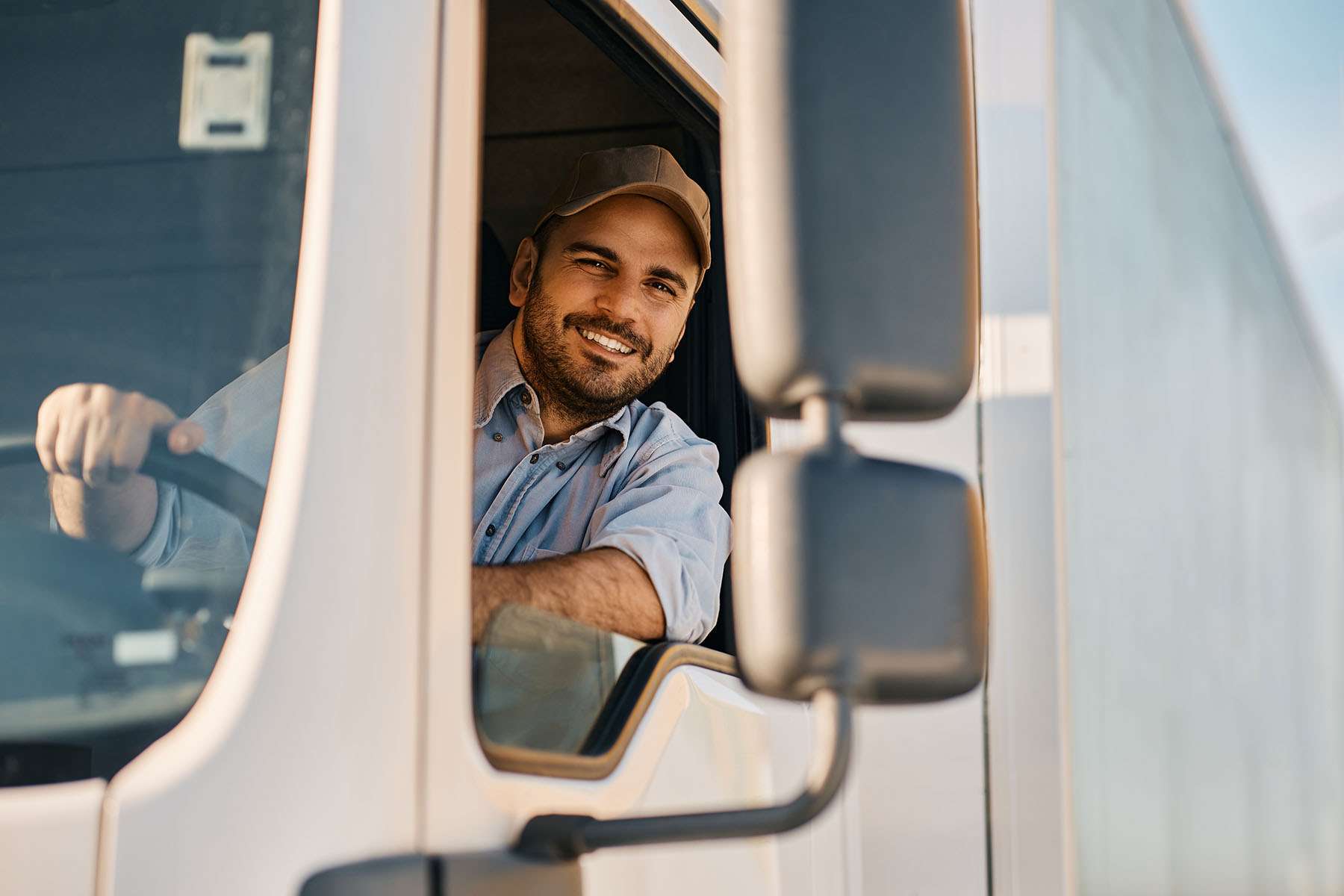 A male driver smiles from the inside of a semi-truck cab.