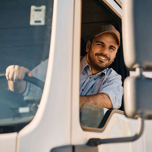 A male driver smiles from the inside of a semi-truck cab.