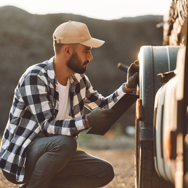A male truck driver inspects the wheels of his truck.