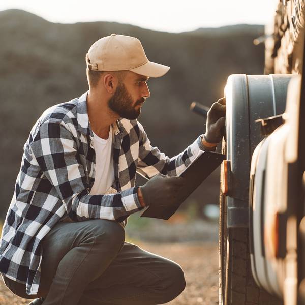 A male truck driver inspects the wheels of his truck.