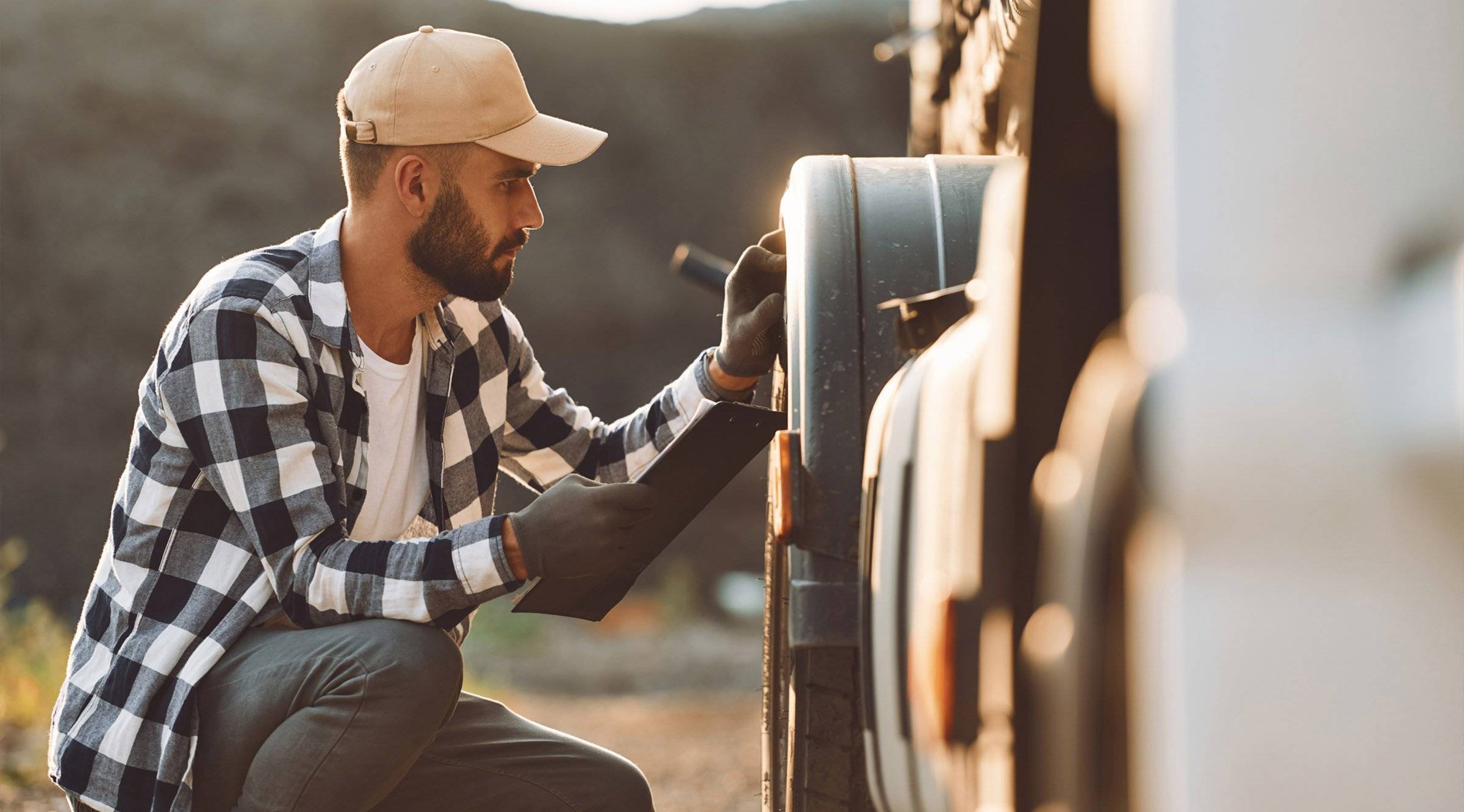 A male truck driver inspects the wheels of his truck.