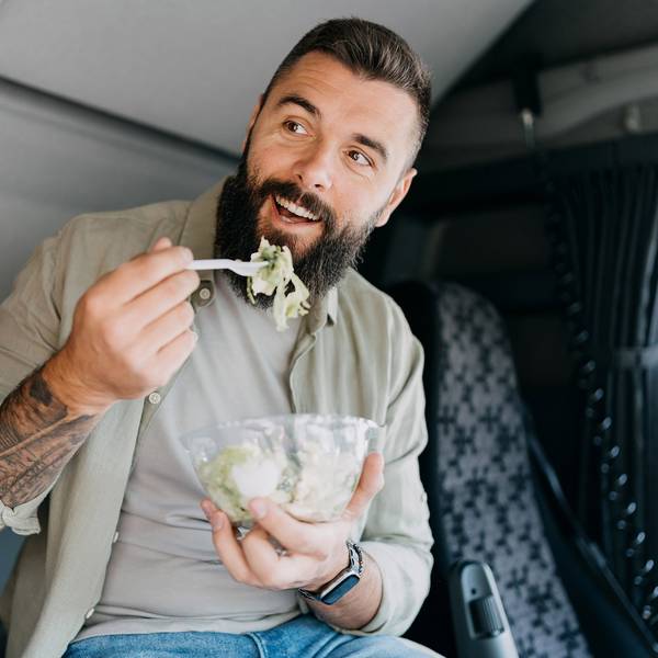A man eats a salad while sitting in the cab of a semi-truck.