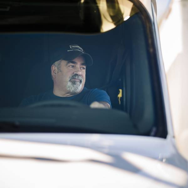 A man in a blue Penske hat sitting behind the wheel of a white truck.