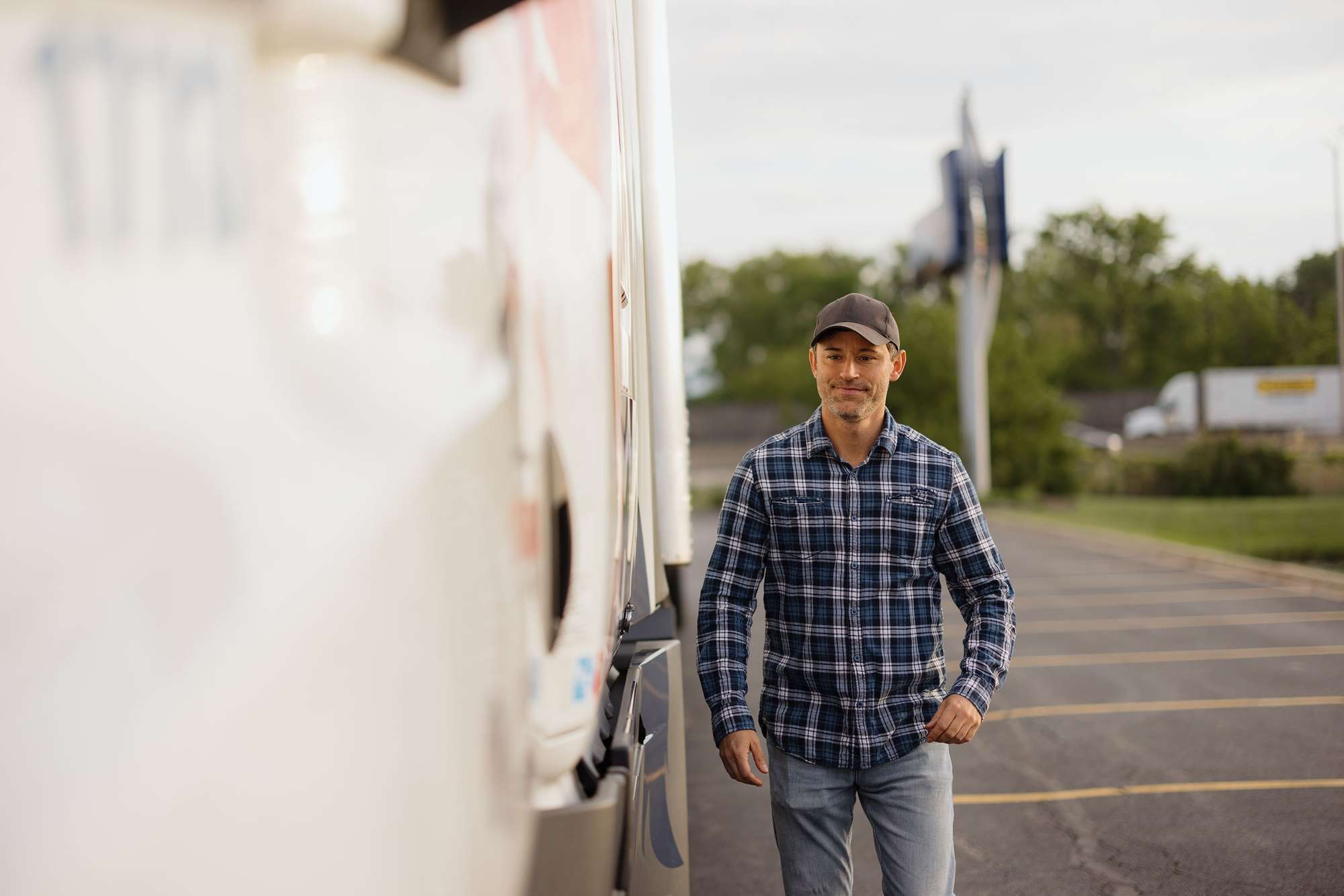 A man in a blue plaid flannel shirt walks in a parking lot next to a white semi-truck.