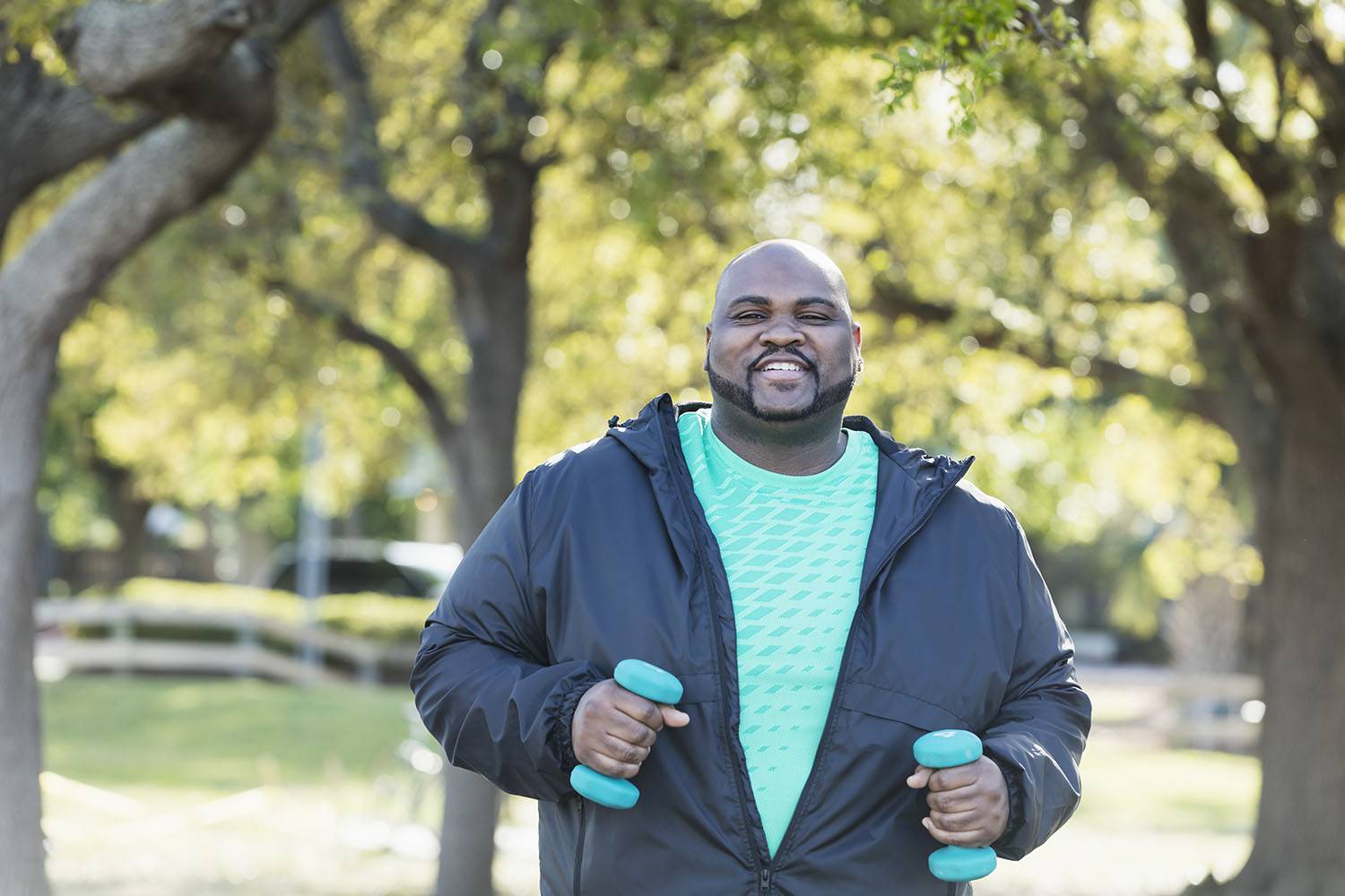 A man in a t-shirt and light jacket walks with blue handweights in his hands.