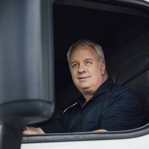 A man sits in the driver seat of a white truck looking out the window.
