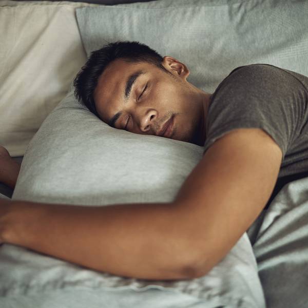 A man sleeps in bed hugging a grey pillow.