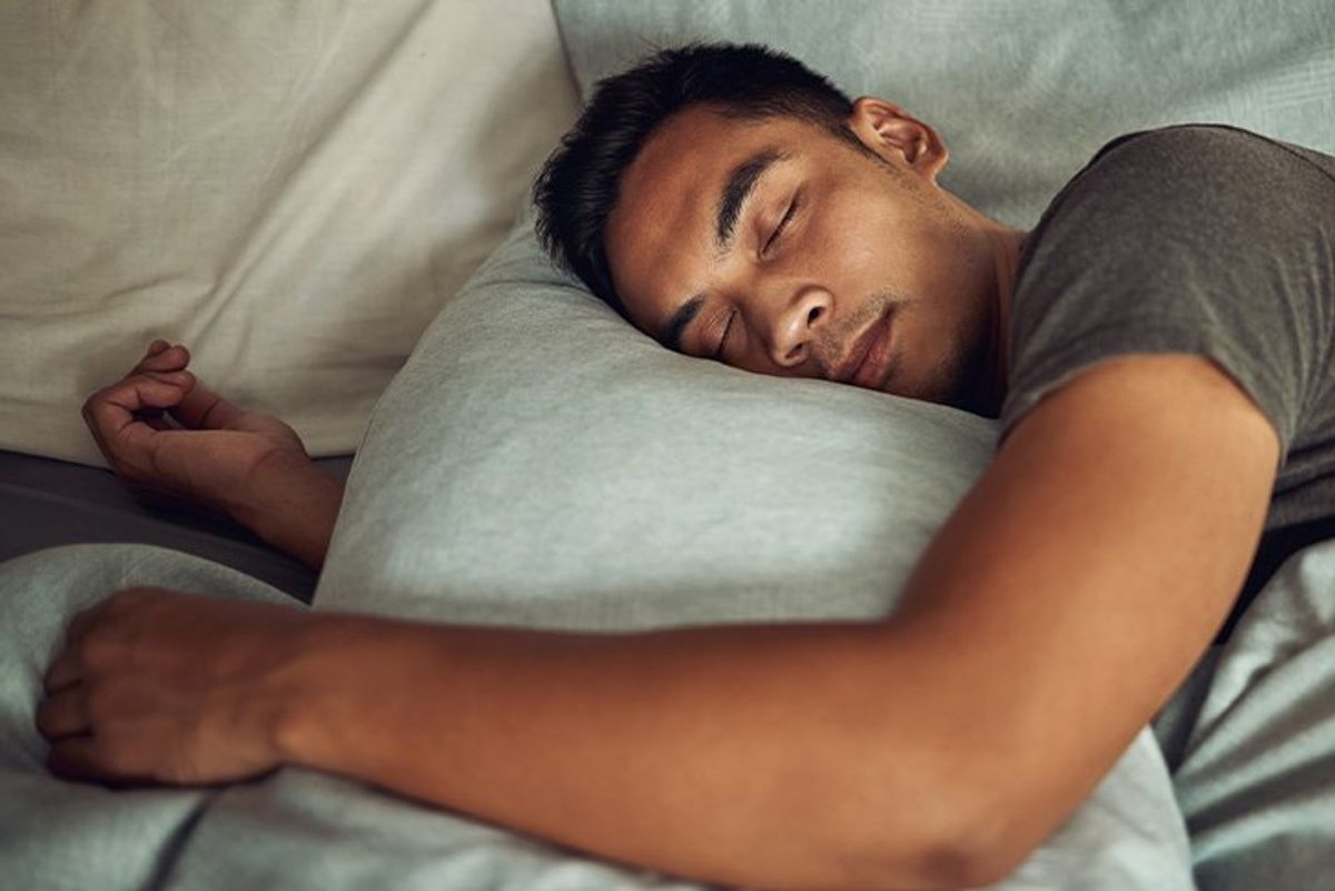 A man sleeps in bed hugging a grey pillow.