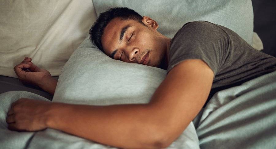 A man sleeps in bed hugging a grey pillow.