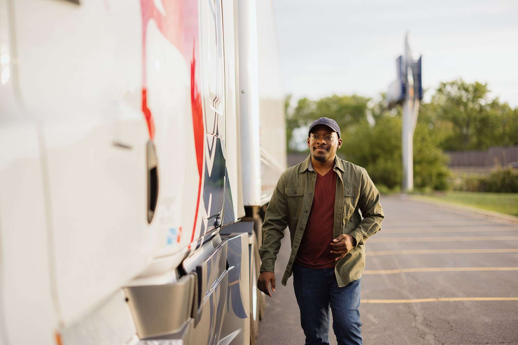 A man walks in a parking lot next to a white and red semi-truck.
