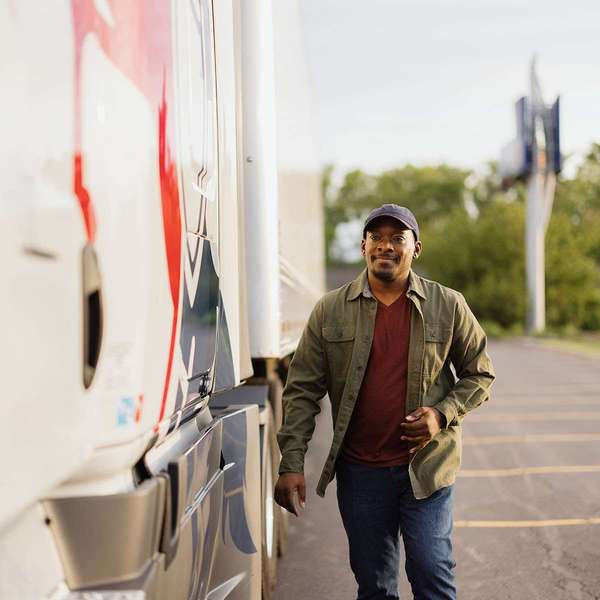 A man walks in a parking lot next to a white and red semi-truck.