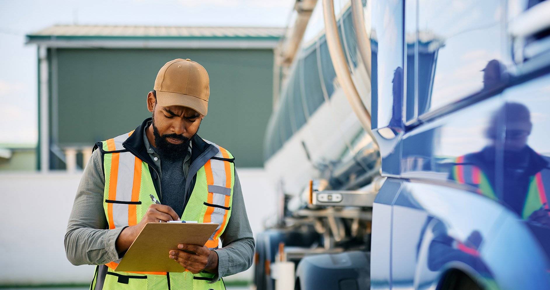 A man walks next to a semi-truck holding a clipboard and pen.