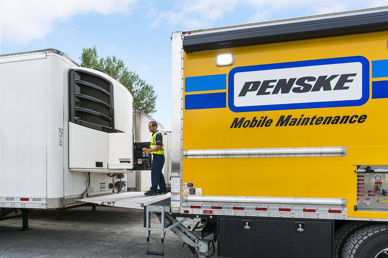 A mobile maintenance technician works on a white refrigerated trailer.
