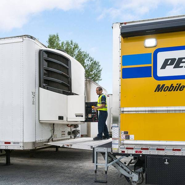 A mobile maintenance technician works on a white refrigerated trailer.