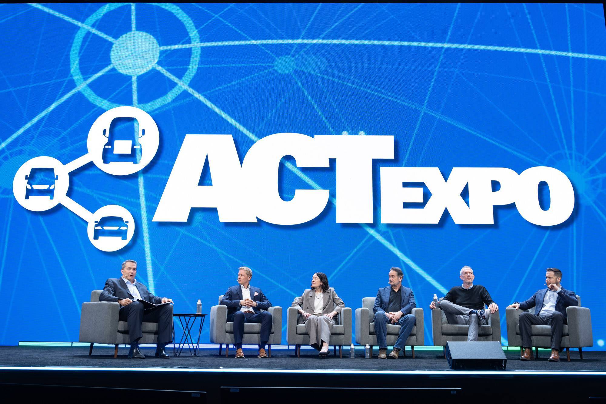 A panel of six people sit on a stage with a blue "ACT EXPO" background.