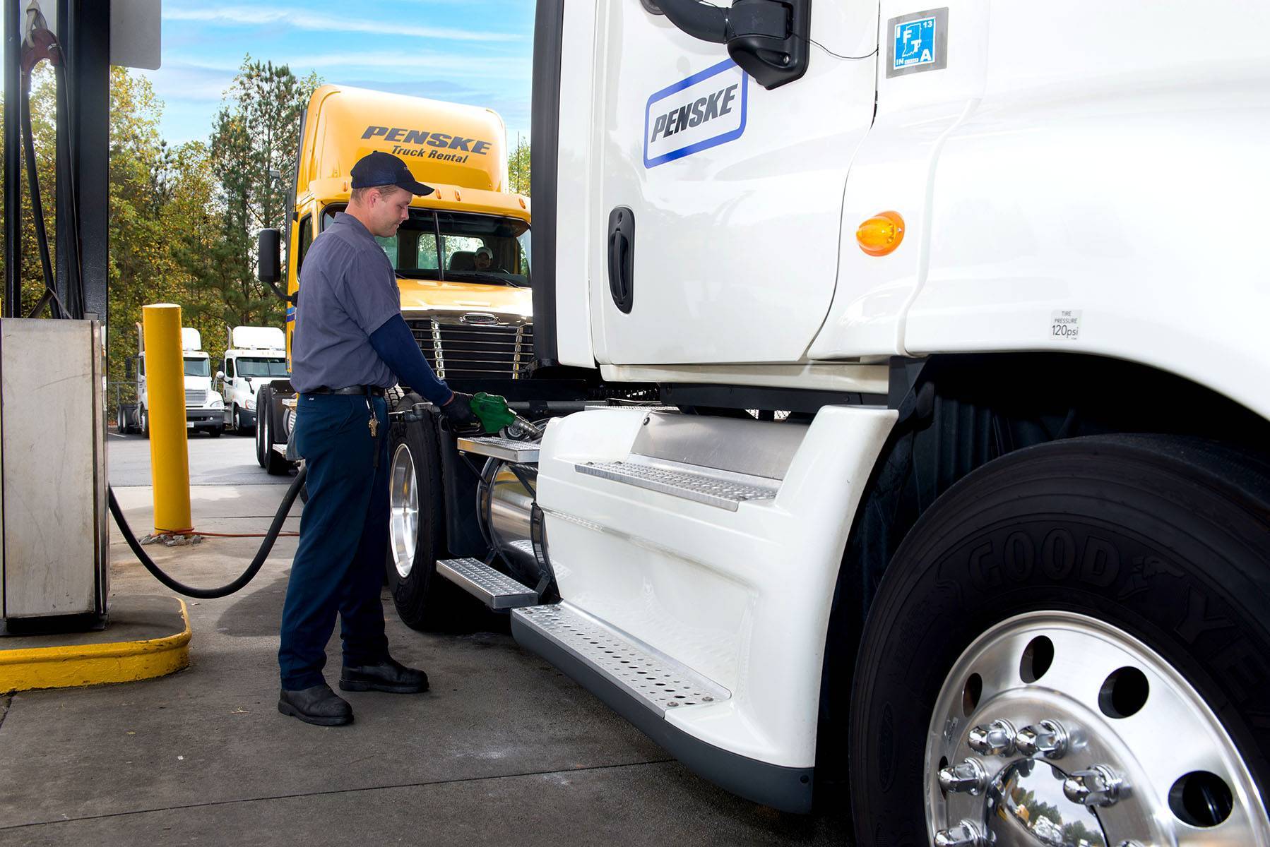 A Penske employee puts fuel into the side of a white Penske semi-truck.