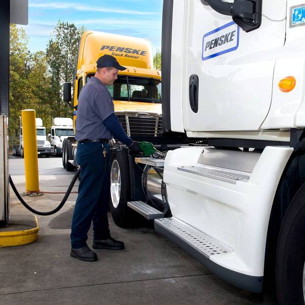 A Penske employee puts fuel into the side of a white Penske semi-truck.