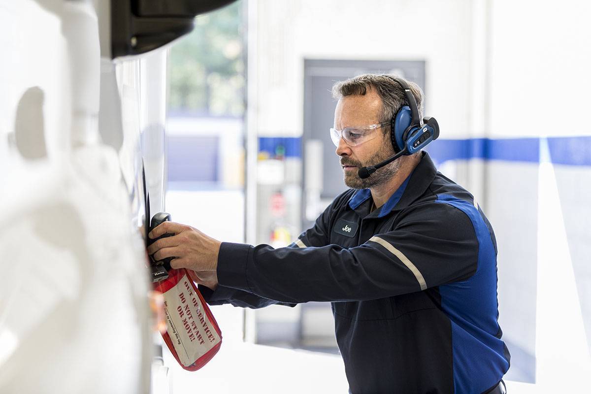 A Penske mechanic in blue works on fixing a truck.