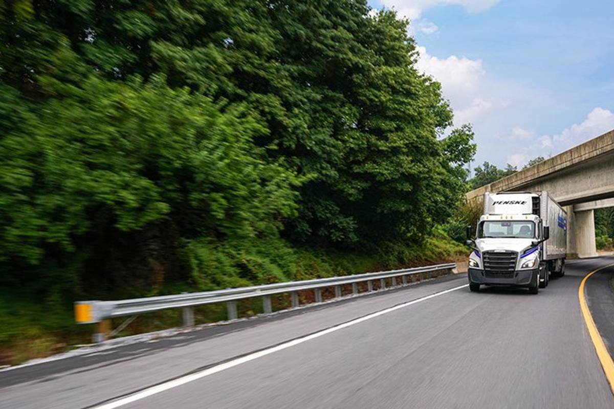 A Penske tractor and refrigerated trailer drive on a road.