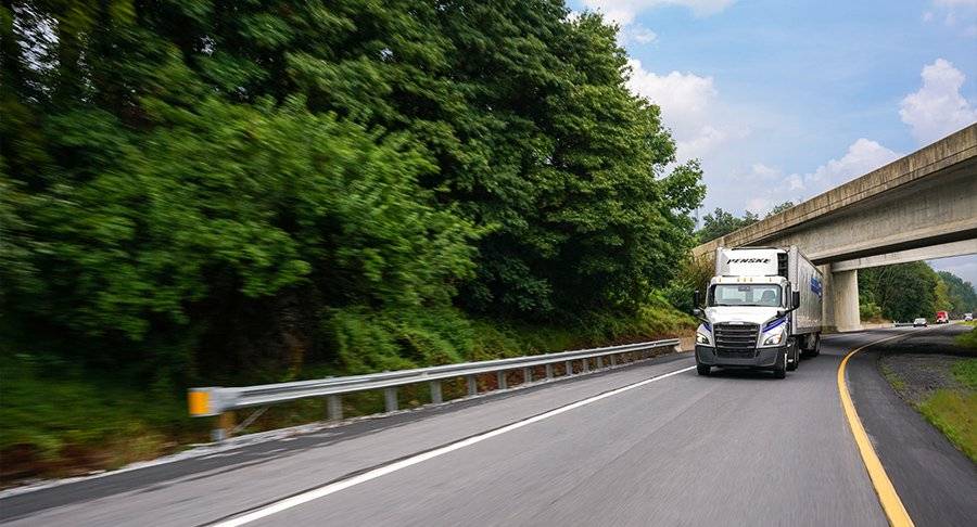 A Penske tractor and refrigerated trailer drive on a road.