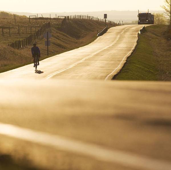 A person rides a bike down a road at sunset with a semi-truck behind.