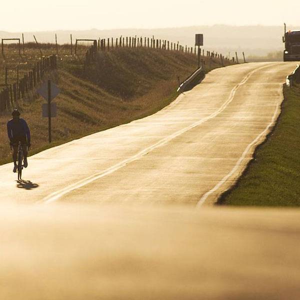 A person rides a bike down a road at sunset with a semi-truck behind.
